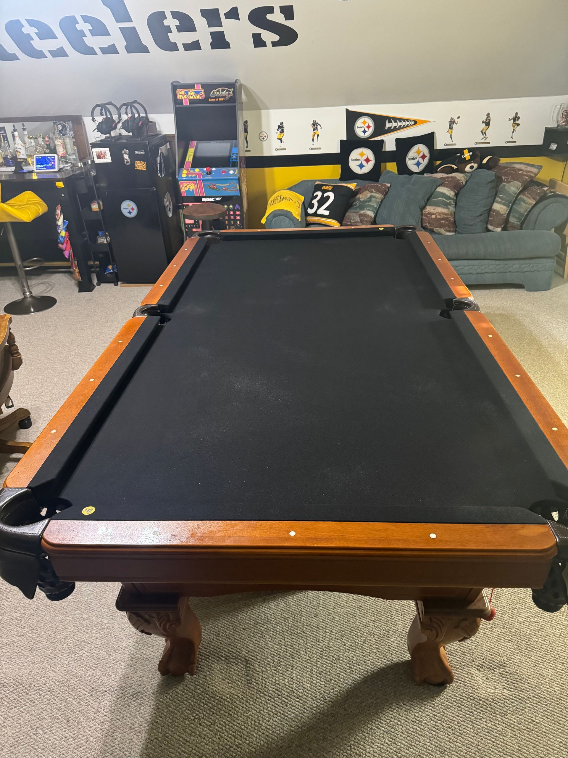 Black pool table in a basement game room with couches and arcade machines behind it