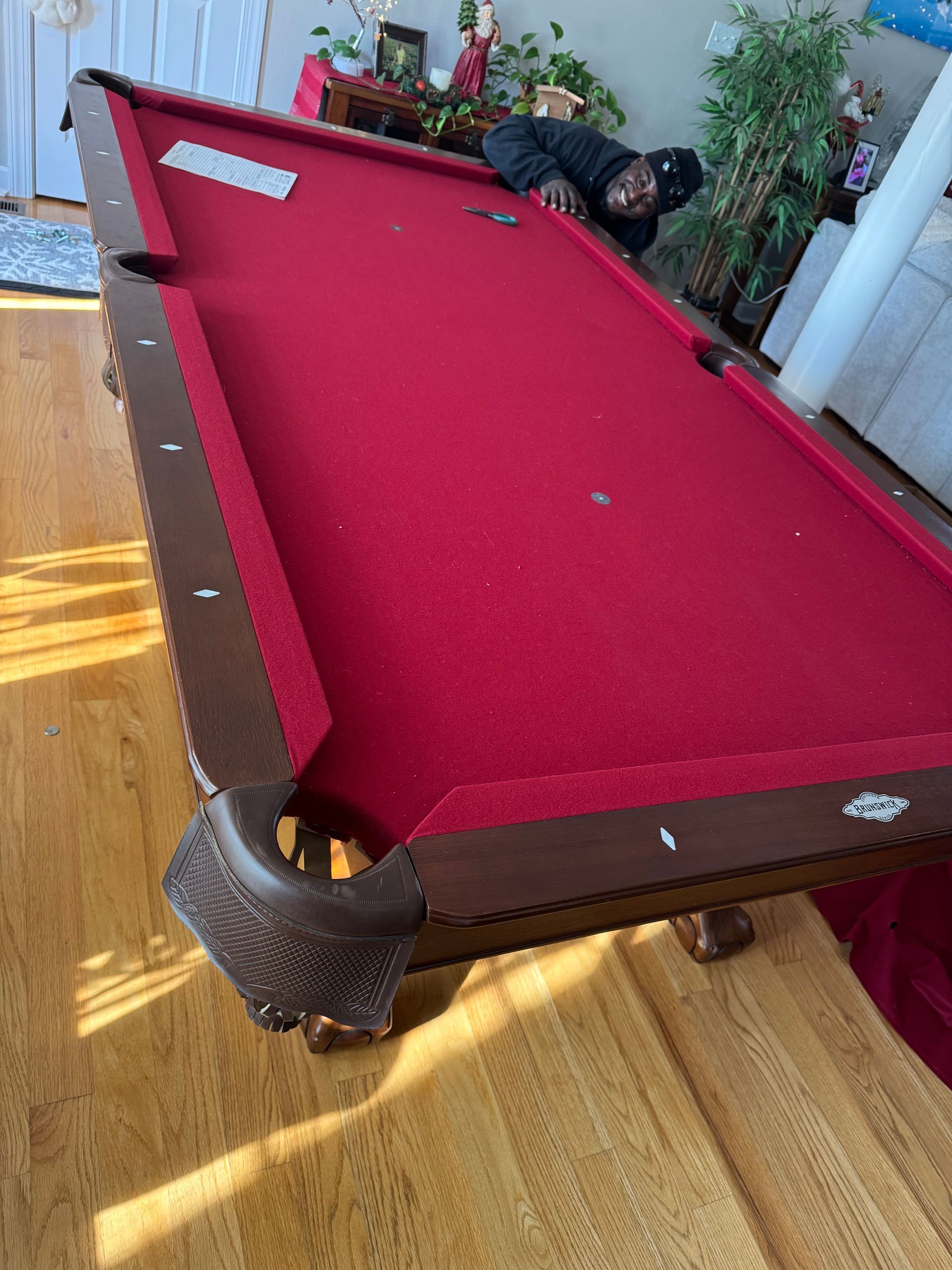 Red pool table with red felt in a sunlit room, with potted plants nearby.