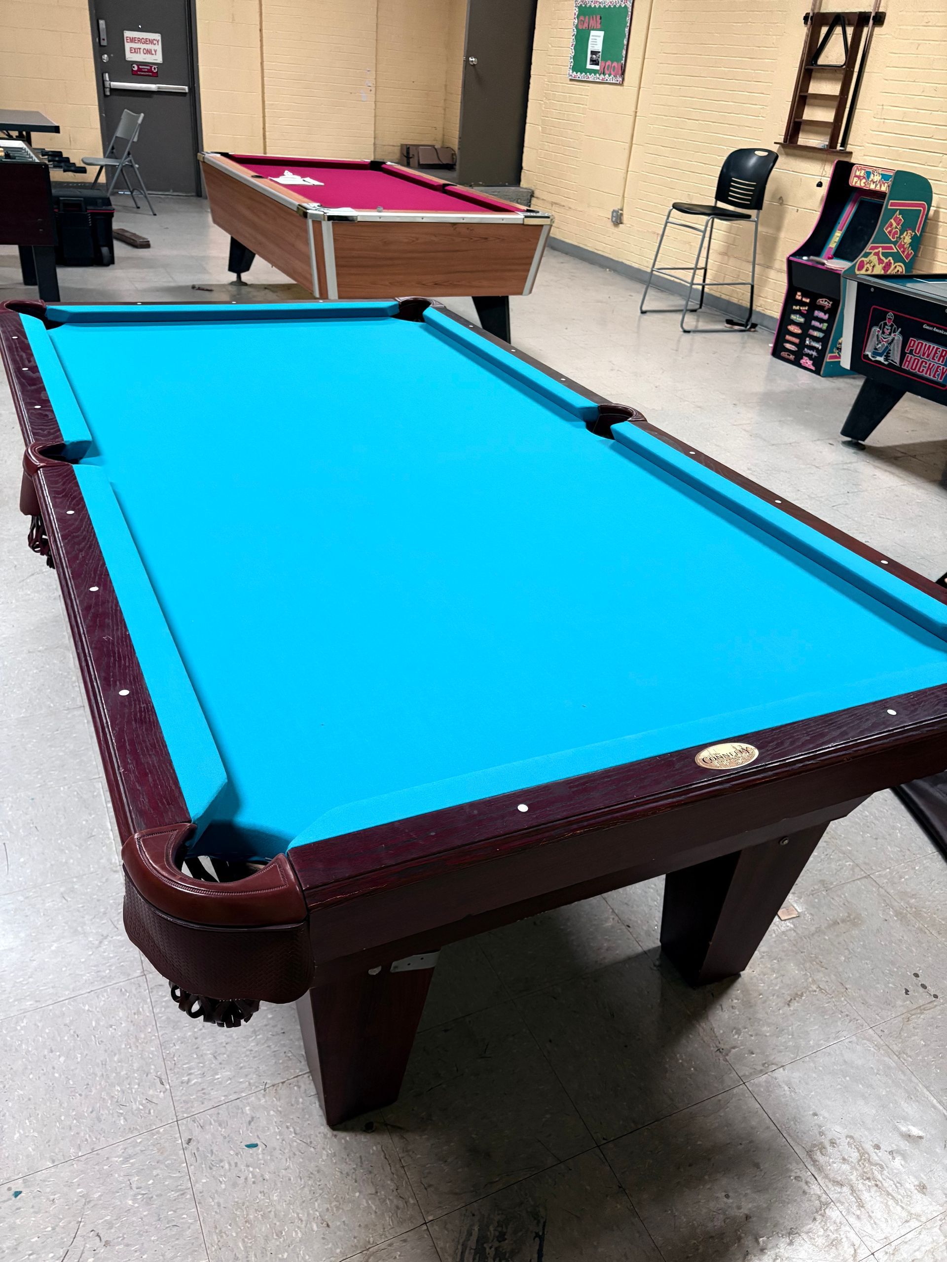 Pool tables in a rec room, with a bright blue felt table in the foreground.