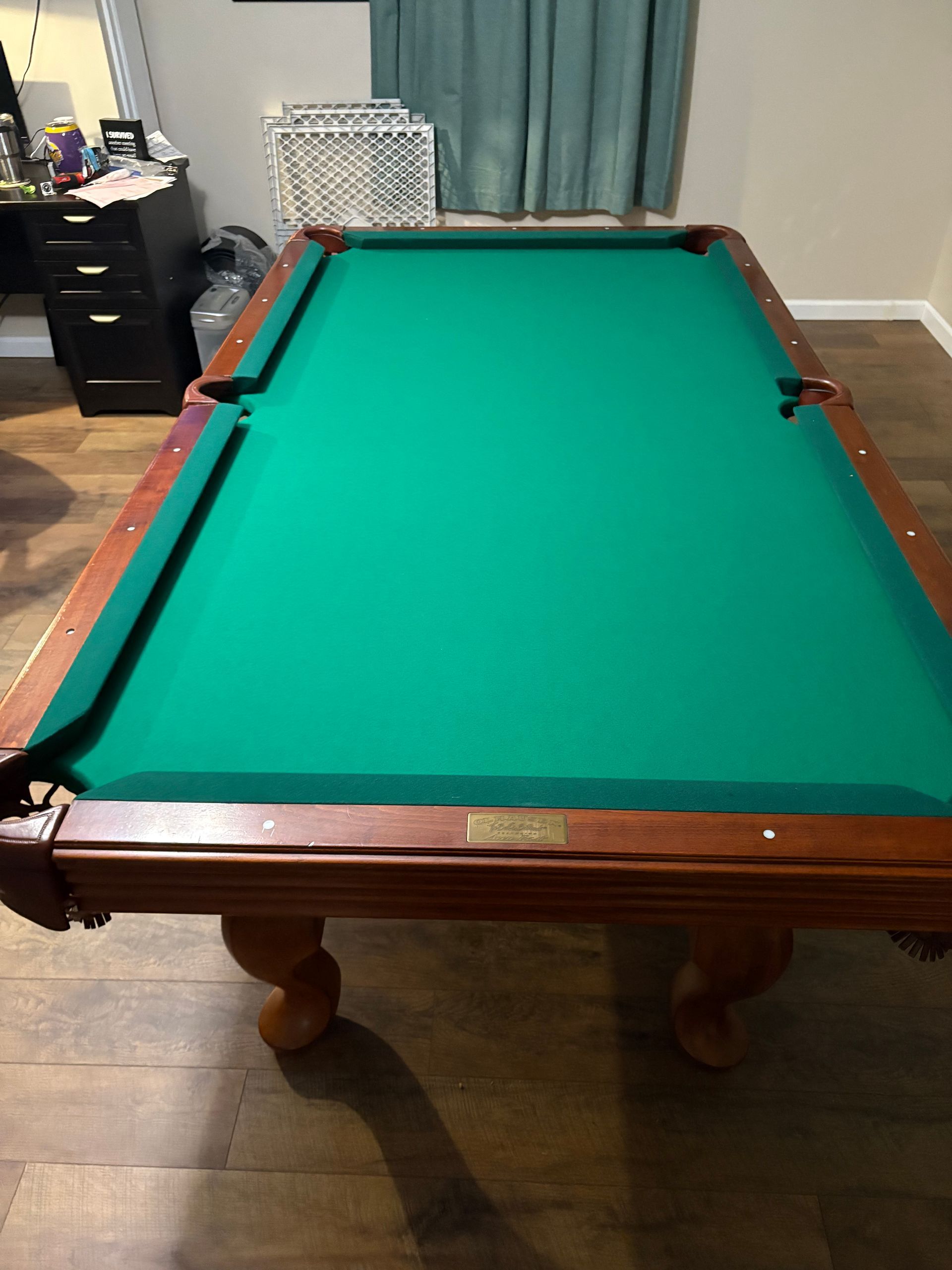 Pool table with green felt in a room with hardwood floors and curtains, viewed from the foot end