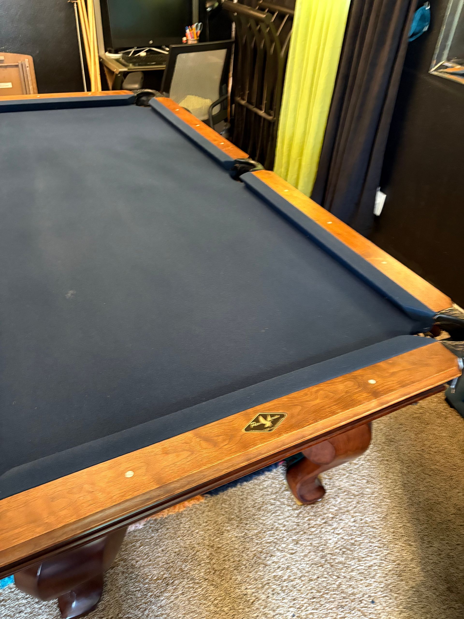 Dark blue pool table with wooden rails in a game room, viewed from a corner.