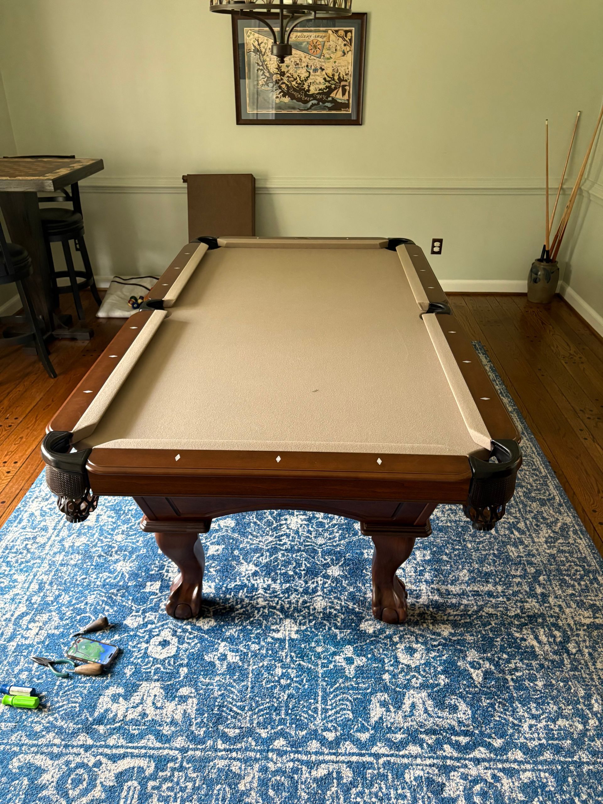 Pool table on a blue rug in a living room with hardwood floors and wall art.