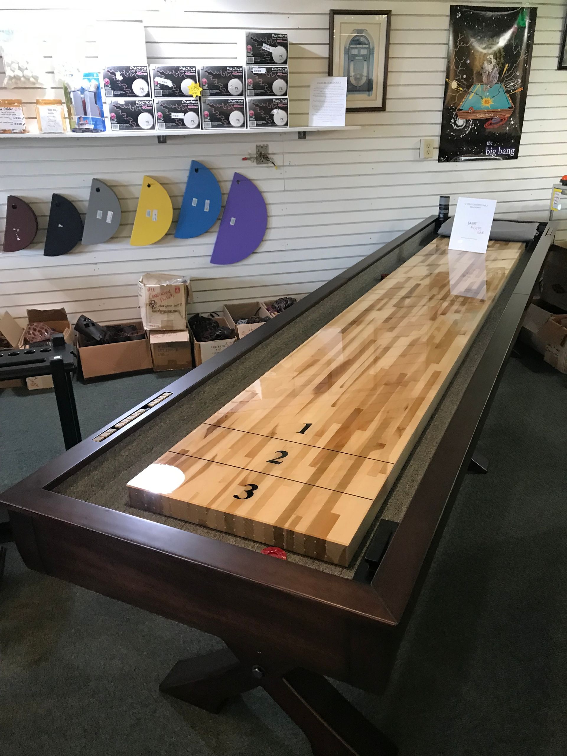 Indoor game room with a long wooden shuffleboard table and wall-mounted accessories displayed behind it.