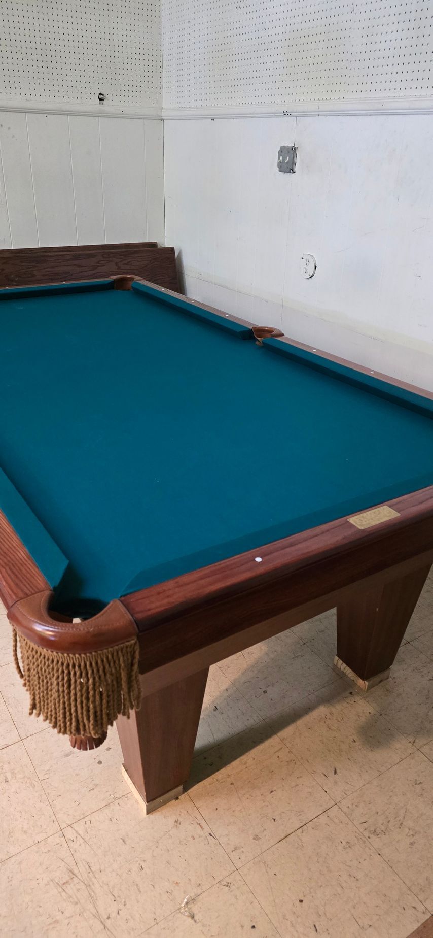 Pool table with teal felt in a sparse indoor room against a white wall