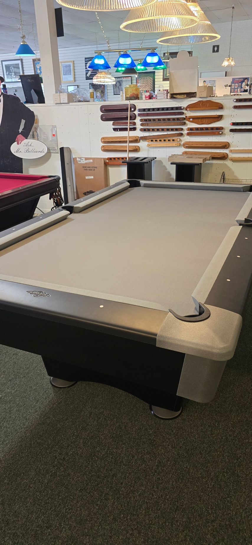Pool table in a store showroom, with shelves and hanging lights in the background.