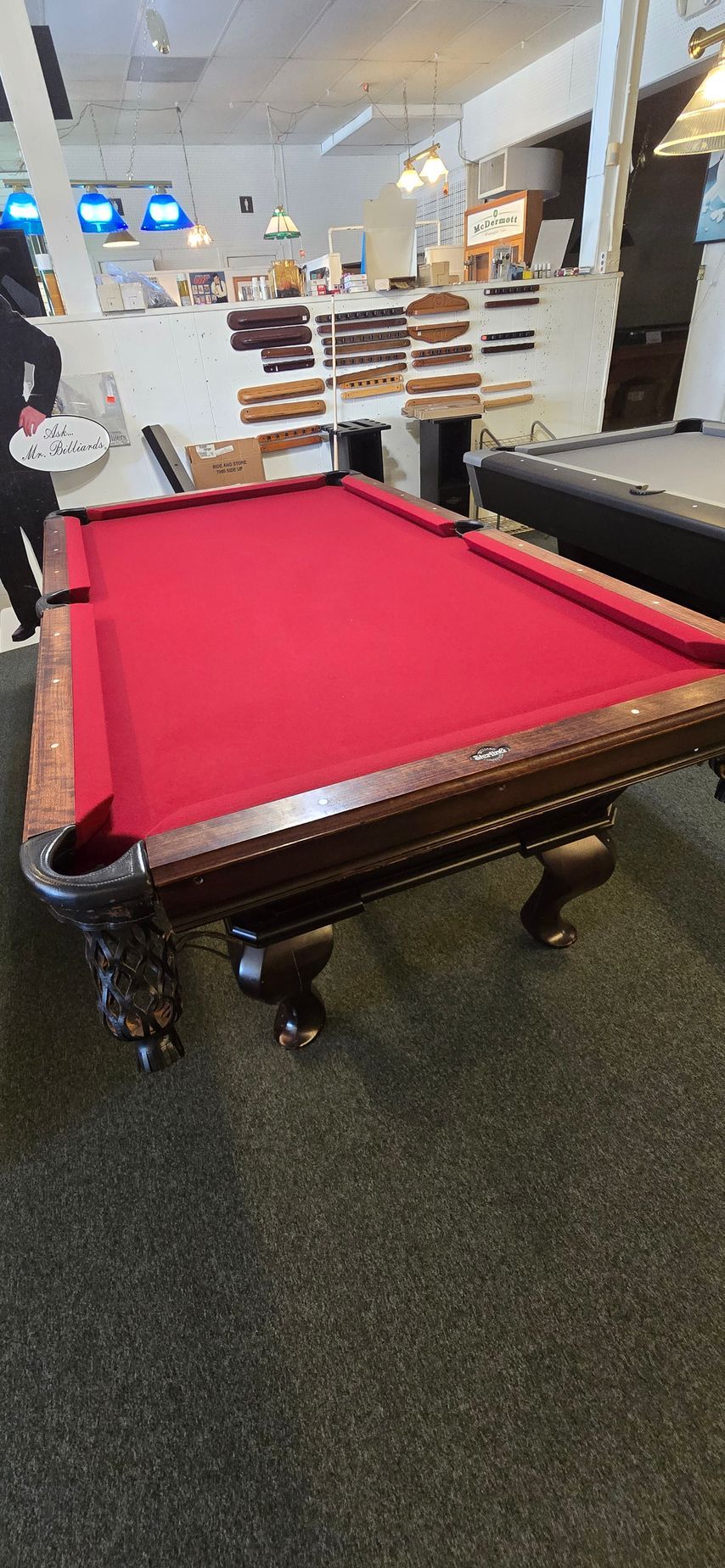 Red-felt pool table in a store or arcade, with shelves and lights in the background.