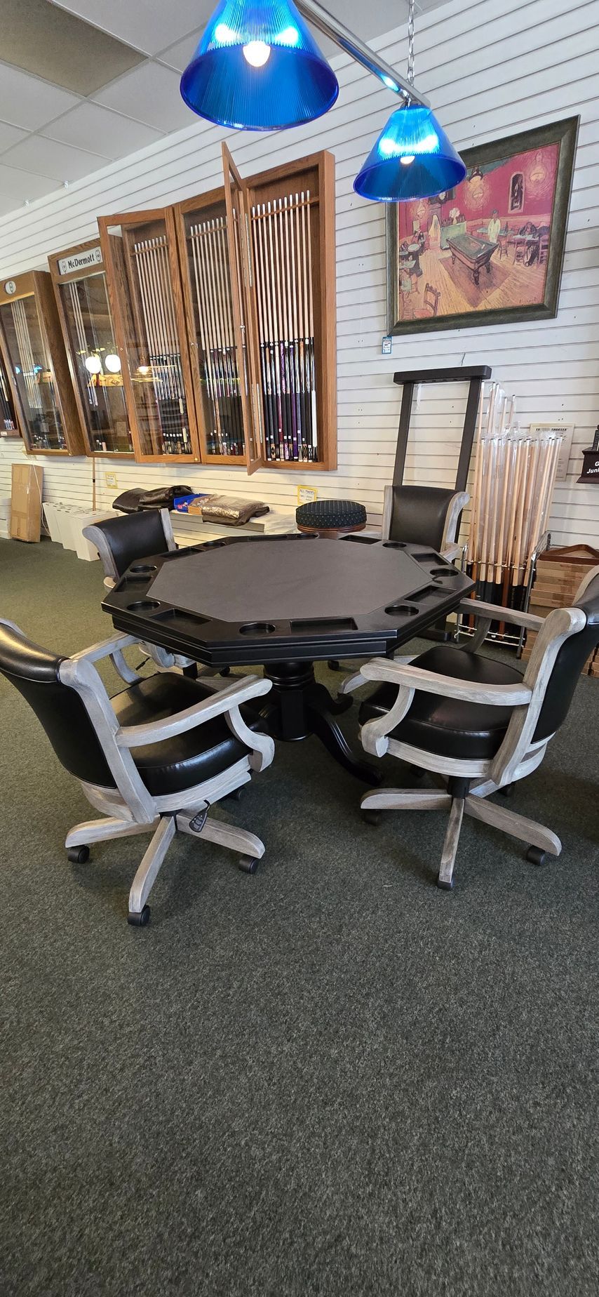 Round black table with four white office chairs in a showroom, under blue hanging lights.