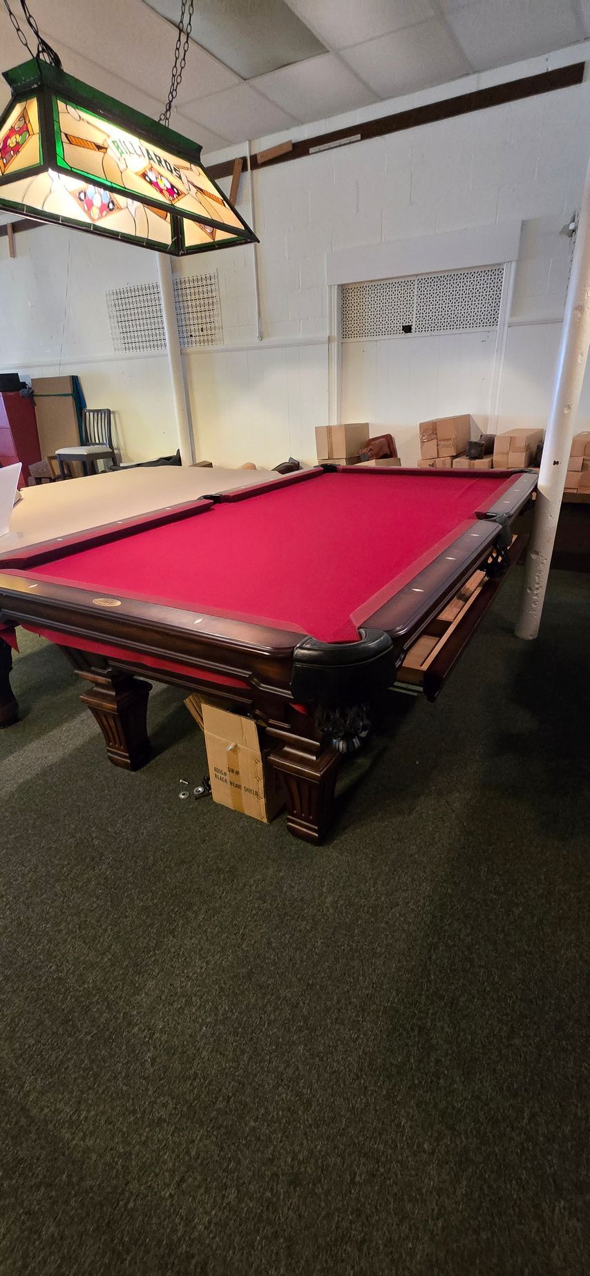 Billiards room with a red-felt pool table under a hanging lamp, a dartboard on the wall, and chairs nearby