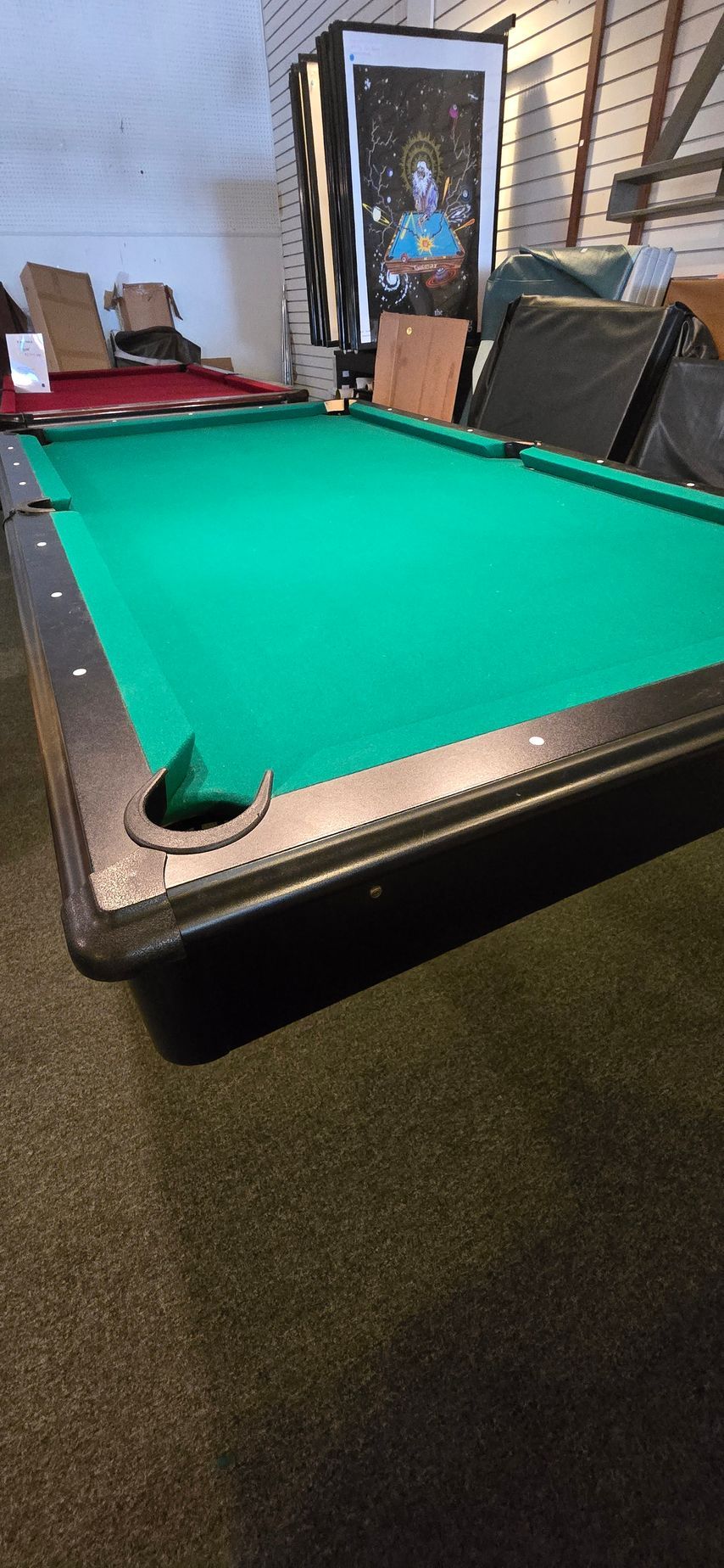 Green-felt pool table in a basement room with chairs and a doorway in the background
