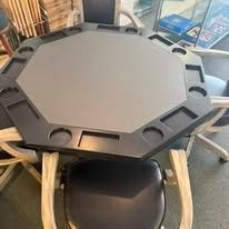 Octagonal black poker table with built-in cup holders in a room with chairs and windows