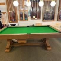 Green billiards table in a room with hanging lights and windows behind it