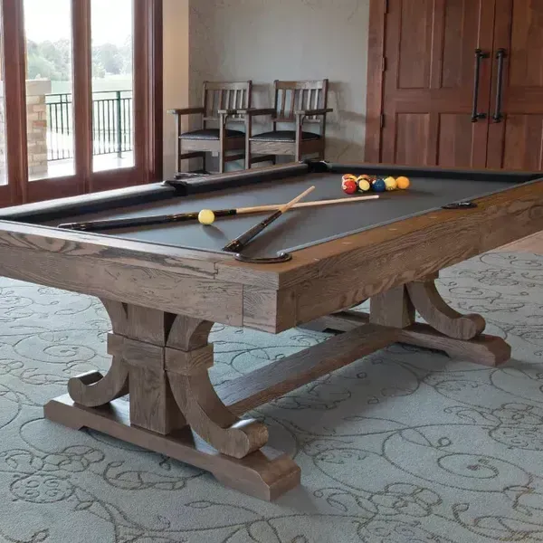 Wooden billiards table with balls and cues in a bright room with windows