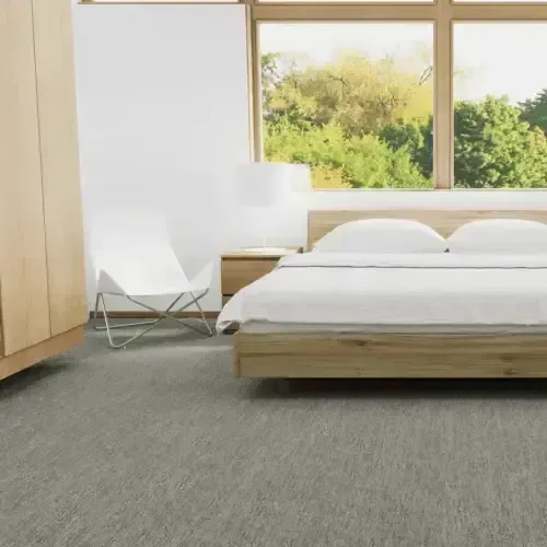 Bedroom with light wooden bed frame, large window, white chair, and gray carpet.