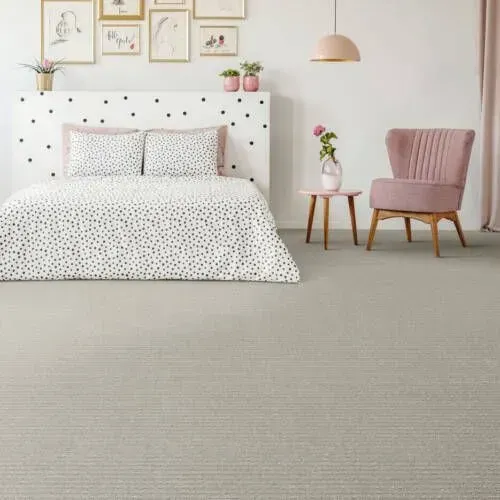 Bedroom with patterned bedding, pink chair, and light gray carpet. Wall art and a pink lamp complete the decor.