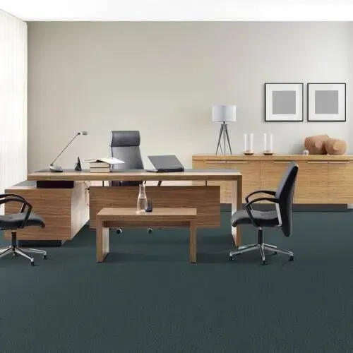 An office with wooden furniture, including a desk, cabinet, and coffee table. Chairs and a lamp are present. The carpet is dark blue.