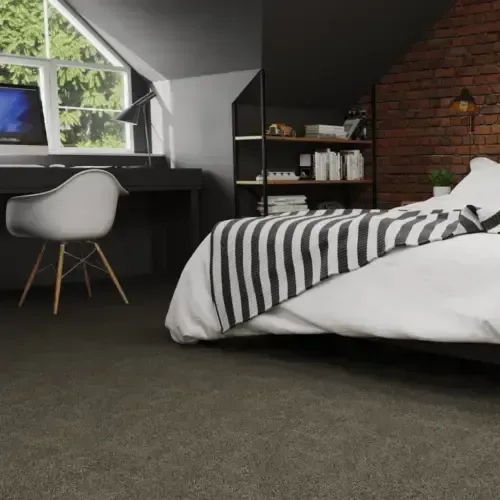 Bedroom with a bed and a desk, featuring a striped blanket, brick wall, and dark carpet.