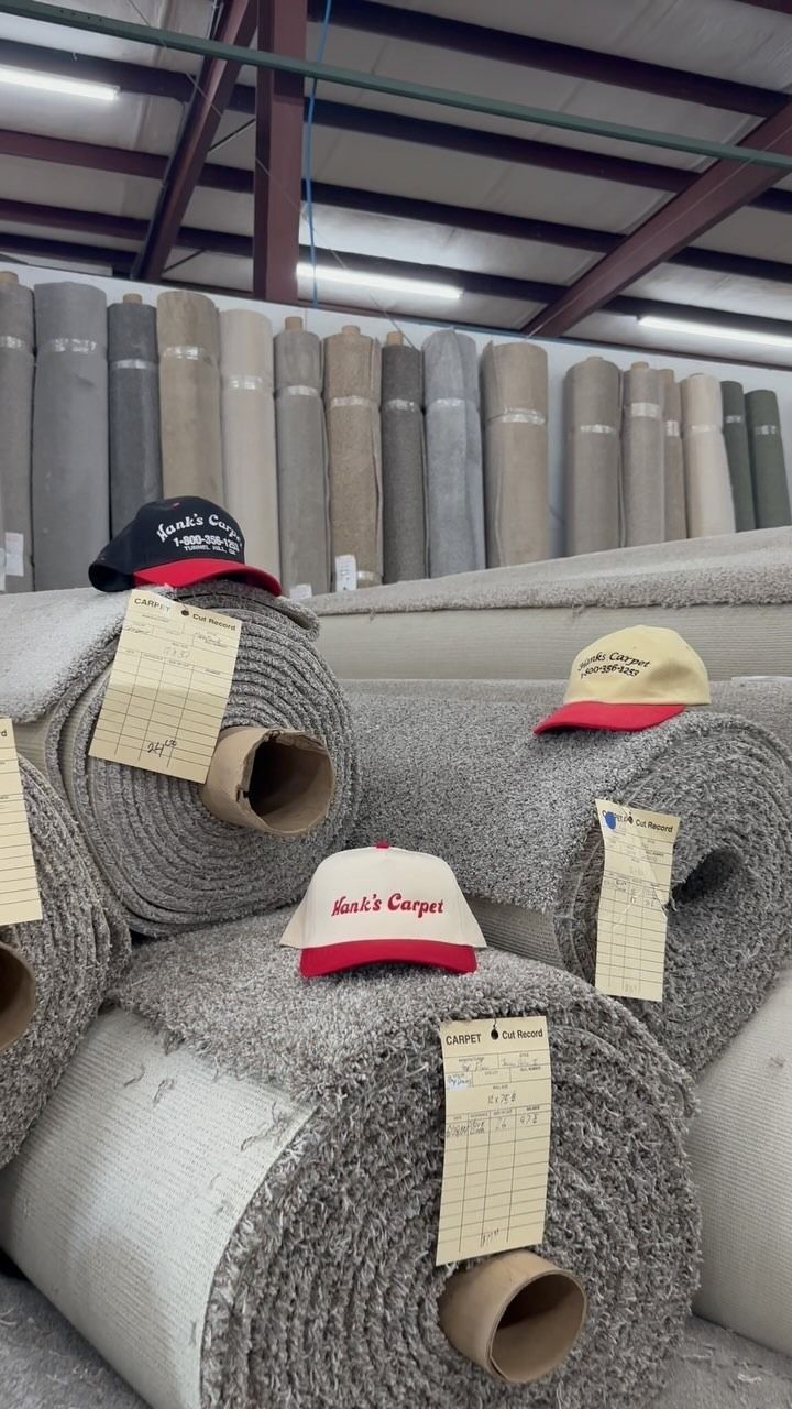 Carpets in rolls stacked in a warehouse. Several hats rest atop the rolls, with price tags attached.