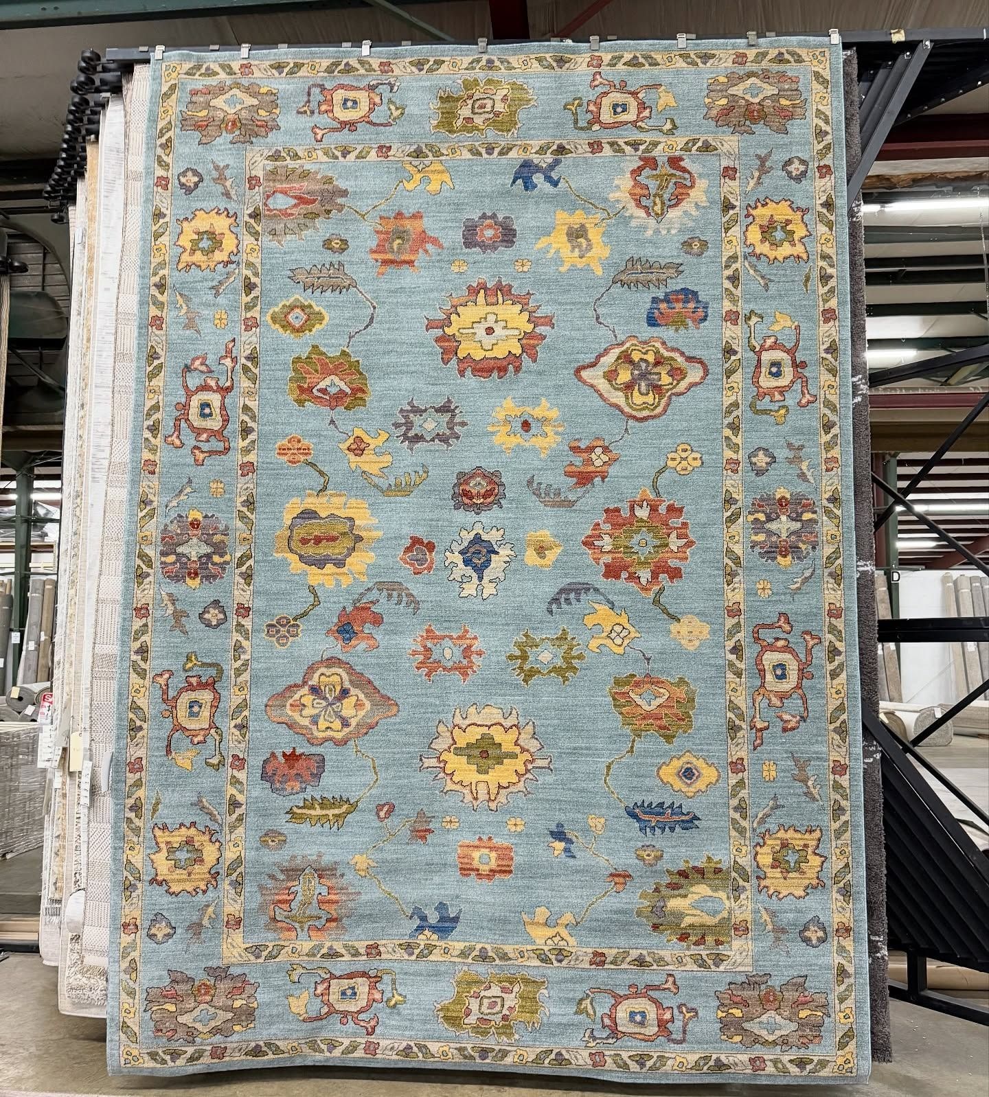 Blue and yellow patterned rug with floral designs hanging in a showroom.