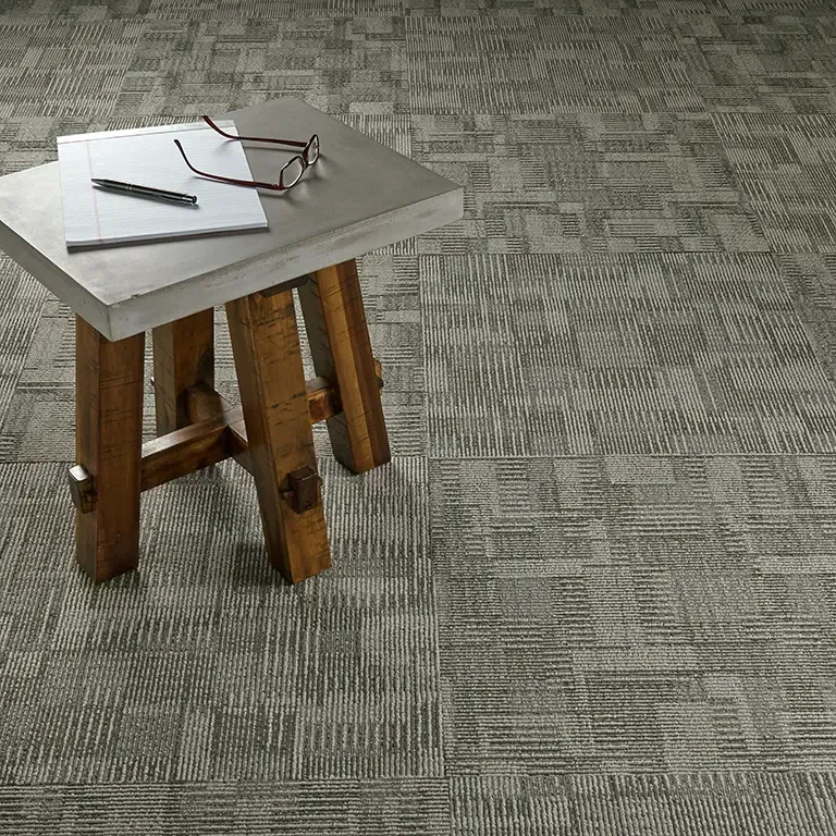 Wooden stool with a concrete top, holding eyeglasses, notepad, and pen on patterned carpet.