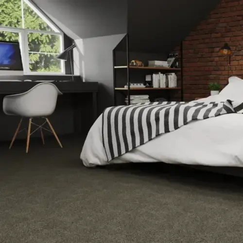 Bedroom with a bed and a desk, featuring a striped blanket, brick wall, and dark carpet.