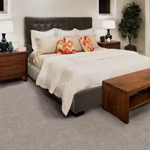 Bedroom with bed, nightstands, lamps, wooden bench, and gray carpet.