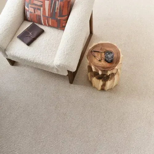 Cozy living room with beige carpet, cream armchair, and wooden side table.