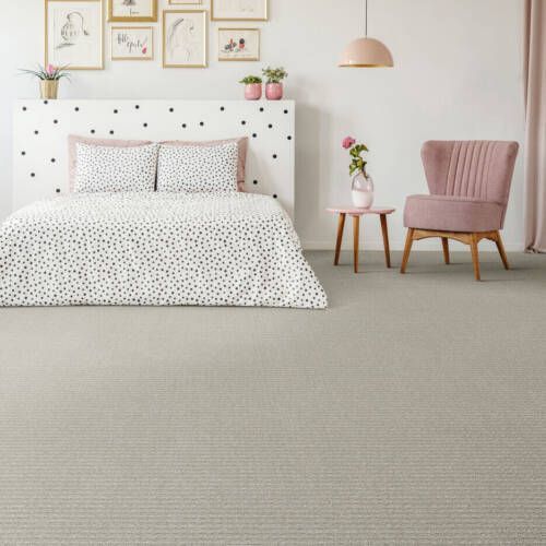 Bedroom with patterned bedding, pink chair, and light gray carpet. Wall art and a pink lamp complete the decor.