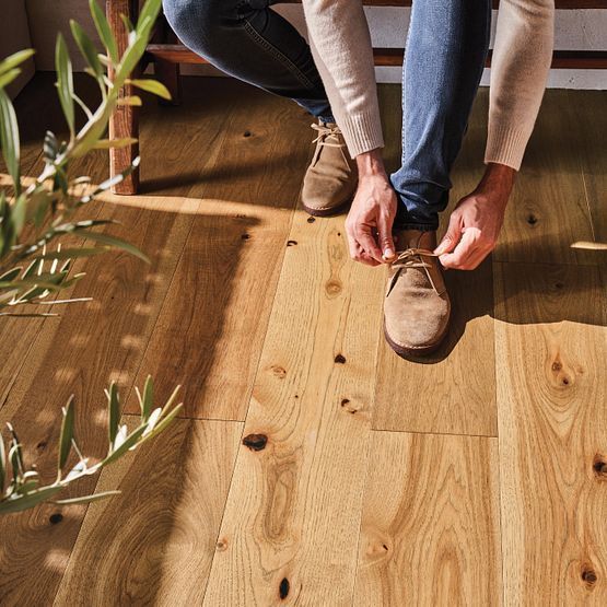 Person tying shoe on a light wood floor.