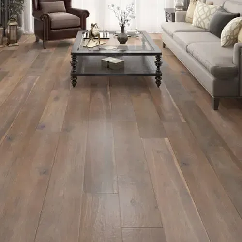 Wooden floor in a living room with a sofa, armchair, coffee table, and vase of flowers.