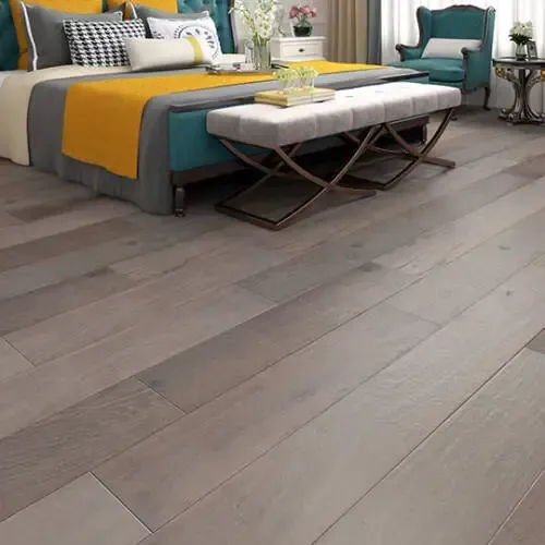 Bedroom with wooden floors, bed, bench, and accent chair. The bed has a yellow and gray blanket.