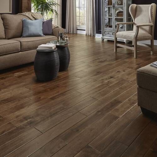 Living room with brown hardwood flooring, sofa, armchair, and black accent tables.