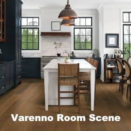 Kitchen with wood flooring, dark cabinets, white island, windows, and hanging copper lights.