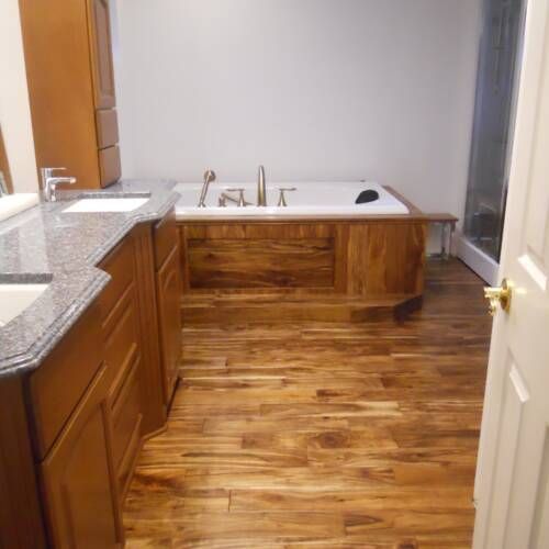 Bathroom with wood flooring, vanity, built-in tub with gold fixtures, and a shower.