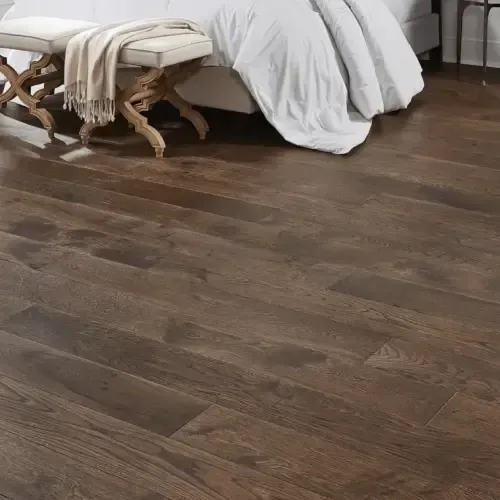 Dark wood flooring in a bedroom, with a bed and bench visible.