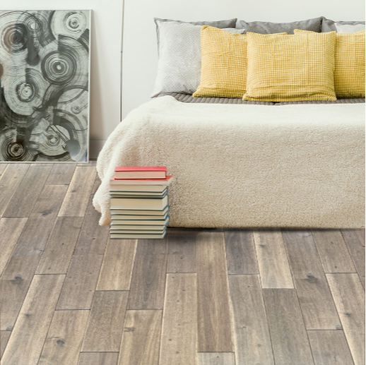 Bedroom with light brown wood floor, bed with yellow pillows, stack of books, and abstract art.