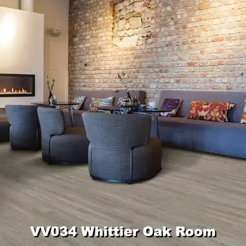 Cozy lounge area with gray seating, a fireplace, exposed brick wall, and wood-look flooring.