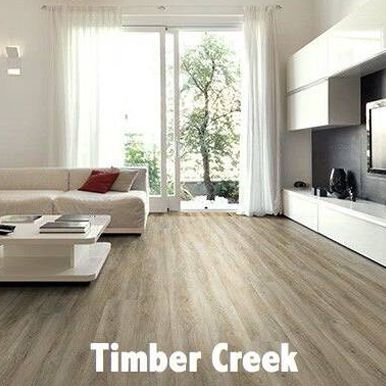 Living room with light wood flooring, white sofa, and large windows with sheer curtains.