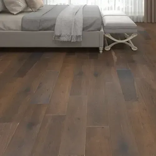 Bedroom with hardwood floor; bed has a grey blanket and pillows; bench at foot of the bed.