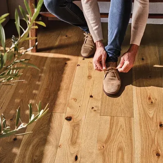 Person tying shoe on a light wood floor.