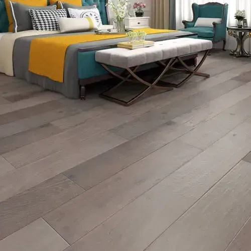 Bedroom with wooden floors, bed, bench, and accent chair. The bed has a yellow and gray blanket.