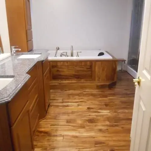 Bathroom with wood flooring, vanity, built-in tub with gold fixtures, and a shower.