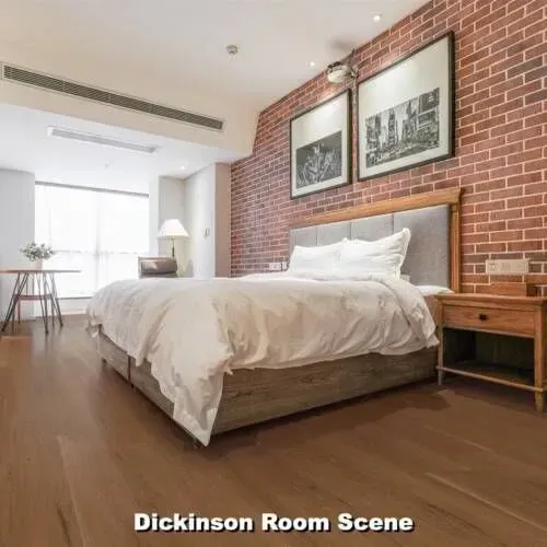 Bedroom with exposed brick wall, bed, nightstand, art, and hardwood floor.