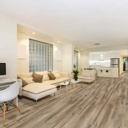Spacious living room with light wooden floors, white walls, and beige furniture.