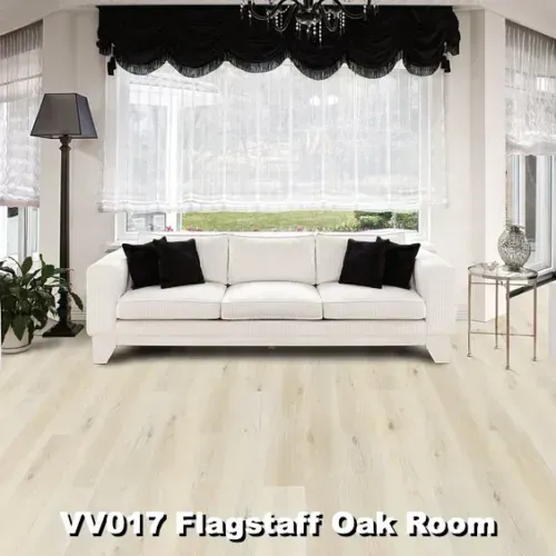 Living room with white sofa, black pillows, and light oak flooring; window behind with light and dark window treatments.