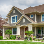 Suburban house with gray siding, white trim, and a covered front porch surrounded by greenery