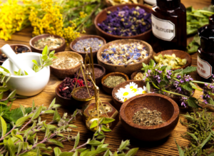 Assorted dried herbs, flowers, and bowls on a rustic table with glass bottles and a mortar and pestle