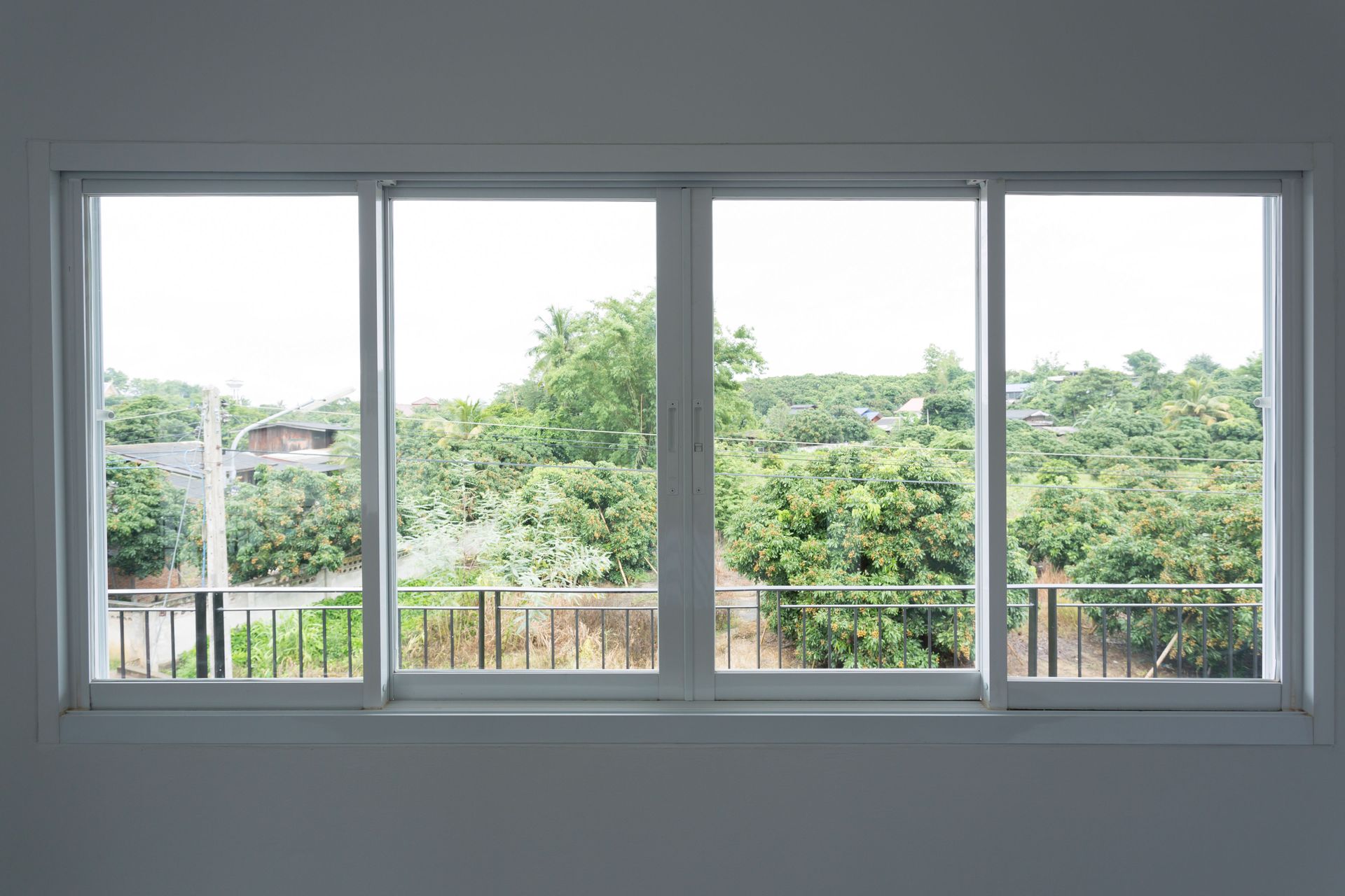 Large white-framed window overlooking green trees and rooftops on a cloudy day
