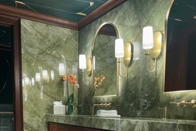 Green marble bathroom with gold accents, arched mirrors, and sconce lighting.