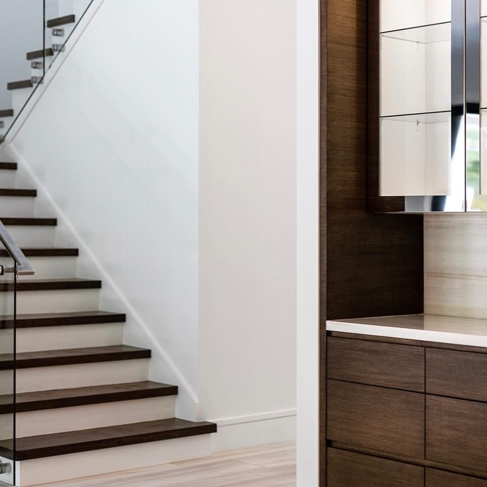 Staircase with dark wood steps and glass railing, next to a dark cabinet with light counter and cabinets