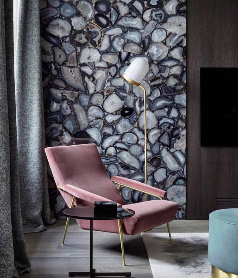 Pink velvet armchair, black side table, gold lamp, and agate stone wall in a modern living room